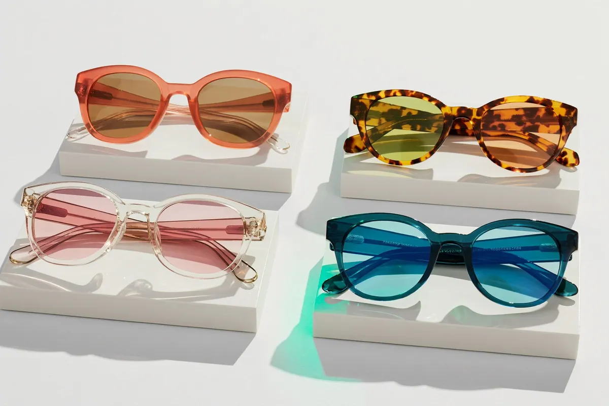 Four colorful pairs of sunglasses — coral, tortoiseshell, rose and teal — arranged on white display blocks