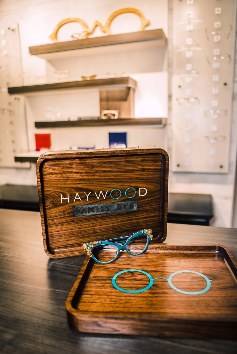 Wooden Haywood Family Eye trays with the teal round-glasses logo, holding a jeweled teal cat-eye frame